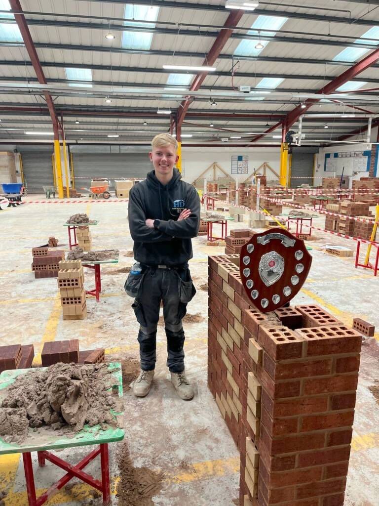 Image of Ellis Smith standing in the brick workshop alongside an award plaque.