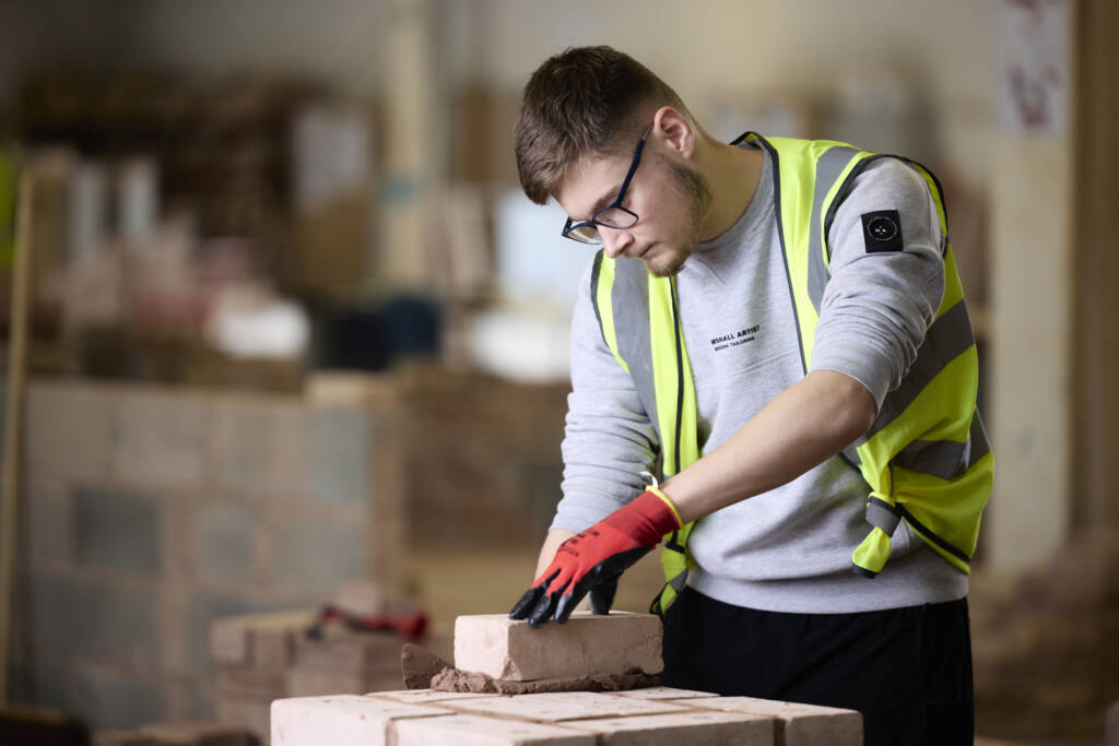 This image depicts an LCB student placing a brick on top of a stack of other bricks.
