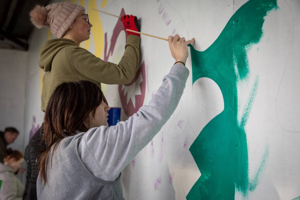 This is a photo of a partially completed mural, currently being worked on by two LCB students.