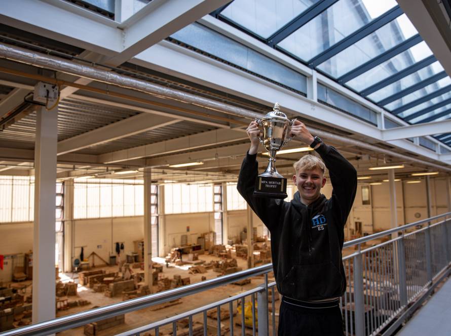 Image of Ellis Smith on the balcony overlooking the brick workshop holding the MPA Mortar trophy.