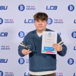 This photo depicts a student with their award against the LCBU photo wall.