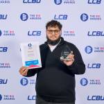 This photo depicts a student with their award against the LCBU photo wall.