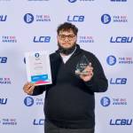 This photo depicts a student with their award against the LCBU photo wall.