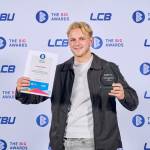 This photo depicts a student with their award against the LCBU photo wall.
