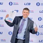 This photo depicts a student with their award against the LCBU photo wall.