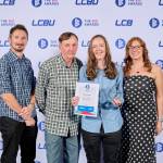 This photo depicts a student with their award against the LCBU photo wall.