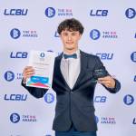 This photo depicts a student with their award against the LCBU photo wall.