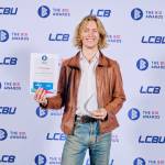 This photo depicts a student with their award against the LCBU photo wall.
