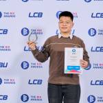 This photo depicts a student with their award against the LCBU photo wall.