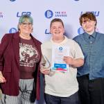 This photo depicts a student with their award against the LCBU photo wall.