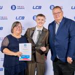 This photo depicts a student with their award against the LCBU photo wall.