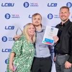This photo depicts a student with their award against the LCBU photo wall.