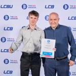 This photo depicts a student with their award against the LCBU photo wall.