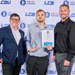 This photo depicts a student with their award against the LCBU photo wall.