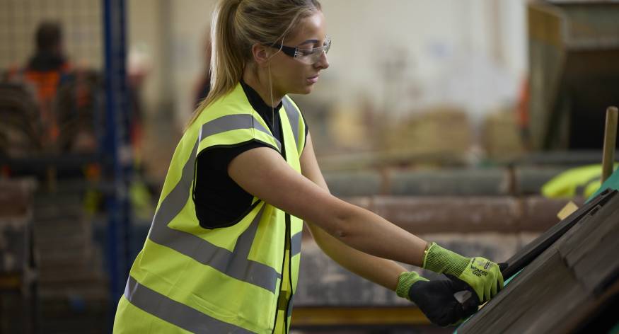 This image depicts a female LCB student placing some roofing tiles on a mock-up roof.