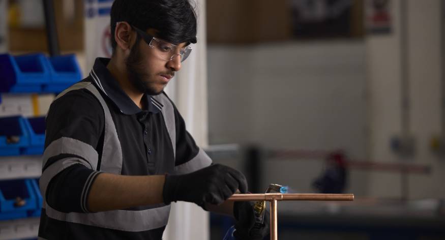 This image depicts an LCB student using a blowtorch on a piece of pipework.